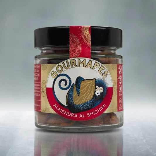 Tarro de almendras tostadas a mano al shichimi. Tarro con diseño moderno y exclusivo Gourmapes, rojo y tonos dorados con un mono azul cogiendo una almendra en el centro.