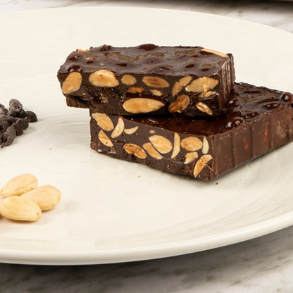 Bandeja de madera con turrón artesanal de chocolate al fondant con almendras Coloma García en envoltorio transparente sobre fondo de estudio.