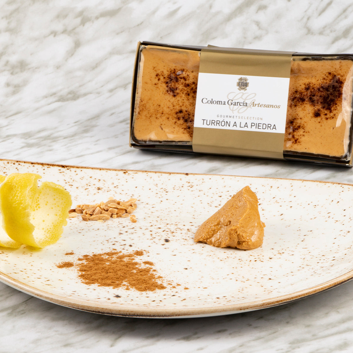 Plato en primer plano con un trozo de turrón a la piedra artesanal Coloma García y tabletón al fondo.