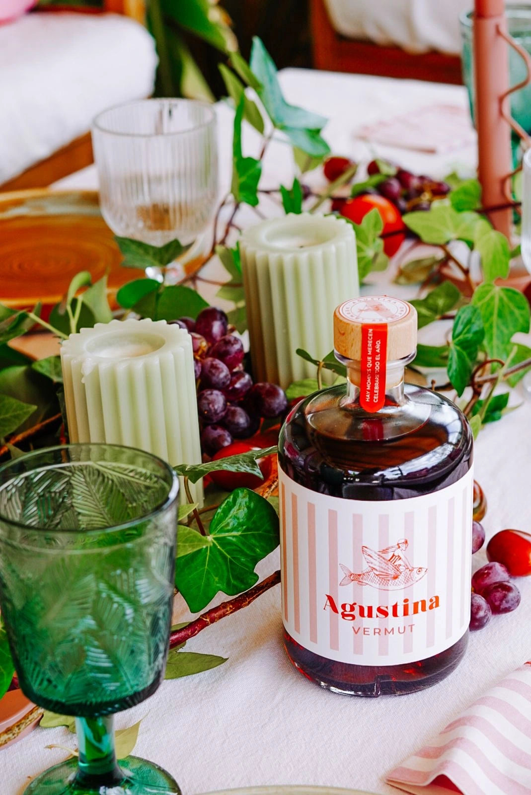 Mesa otoñal decorada con velas, platos y vasos destacando y protagonizando la foto el vermut Agustina, un vermut rojo con un diseño moderno y elegante.