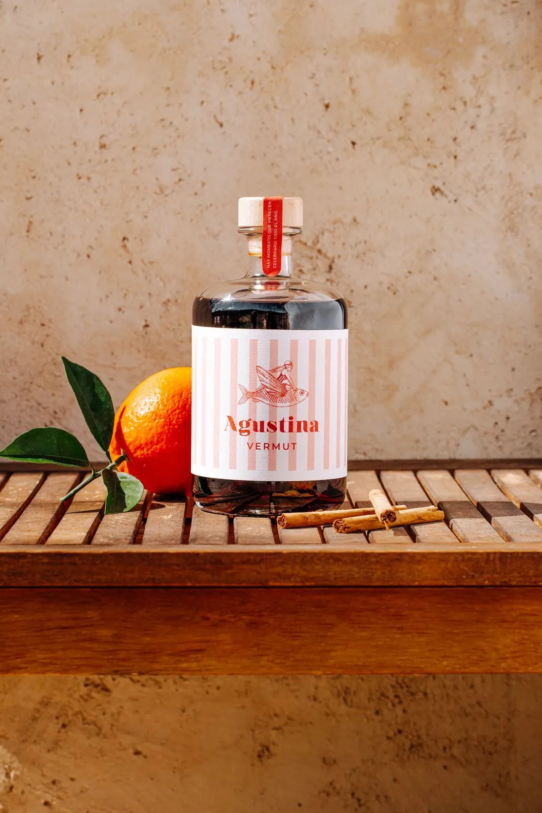 Botella de Vermut Agustina sobre tarima acompañada de una naranja y canela.