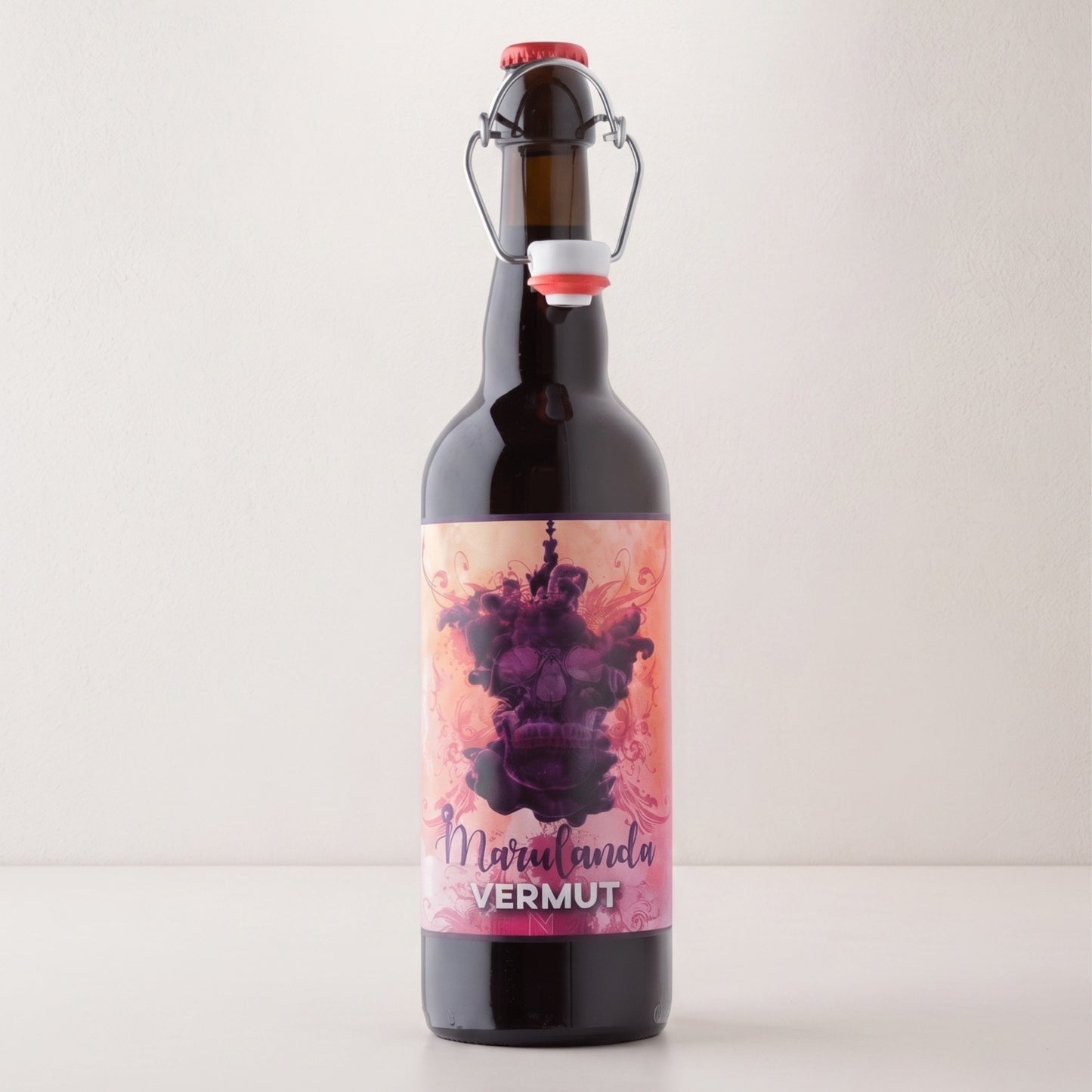 Botella de Vermut Marulanda Rojo artesanal de la Región de Murcia sobre fondo blanco, con cierre mecánico reutilizable y etiqueta rosa ilustrada con una calavera entre humo morado. En la parte inferior destaca el nombre Marulanda en color lila y la palabra Vermut en blanco.