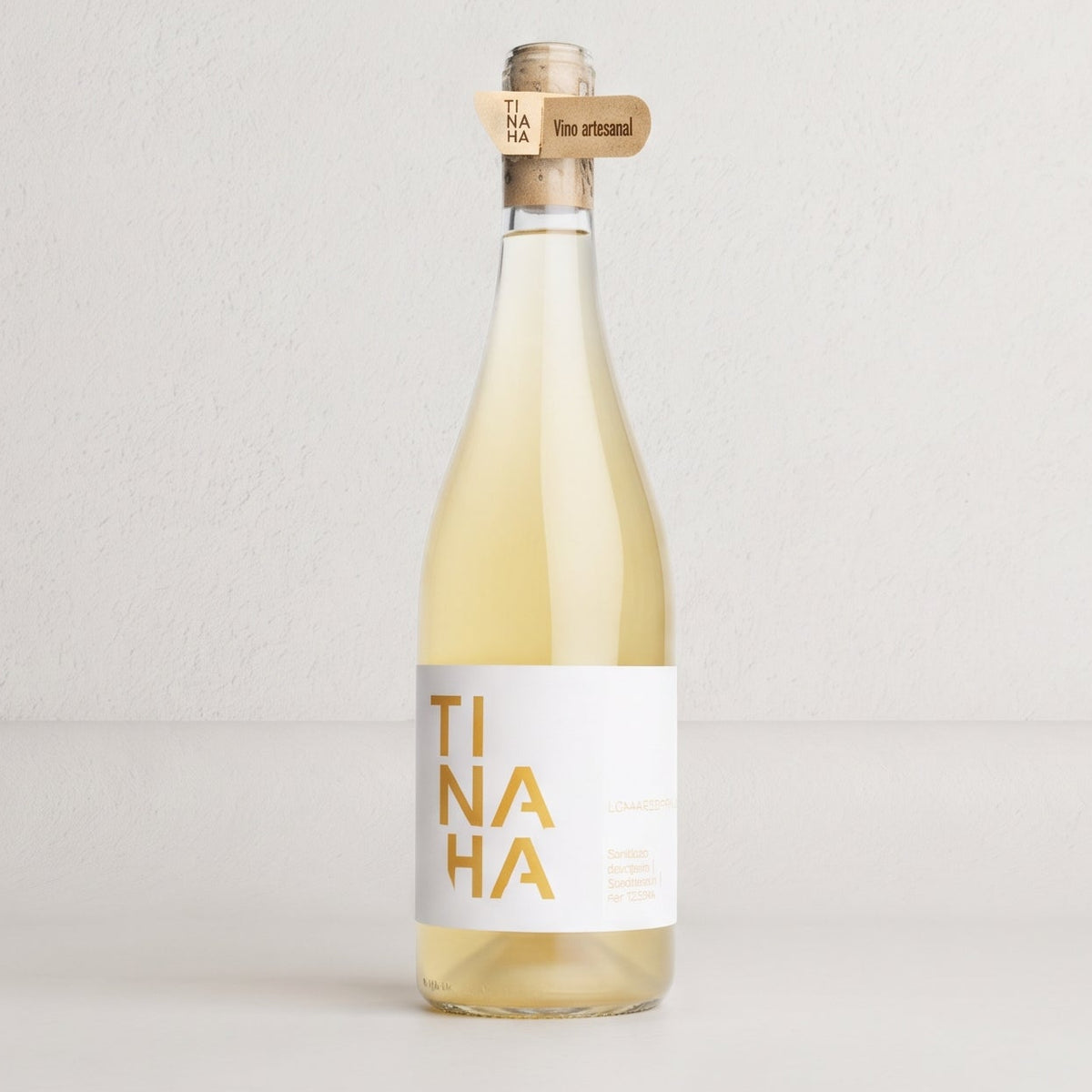 Botella de vino blanco Tinaha sobre fondo de estudio. Formato tradicional con etiqueta blanca en un costado y el nombre «TINAHA» en letras amarillas divididas en tres líneas.