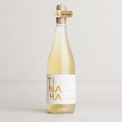 Botella de vino blanco Tinaha sobre fondo de estudio. Formato tradicional con etiqueta blanca en un costado y el nombre «TINAHA» en letras amarillas divididas en tres líneas.
