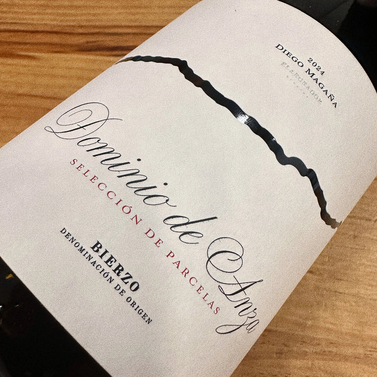 Primer plano de la etiqueta blanca de estilo clásico del vino tinto Dominio de Anza Selección de Parcelas 2024 sobre una mesa de madera.