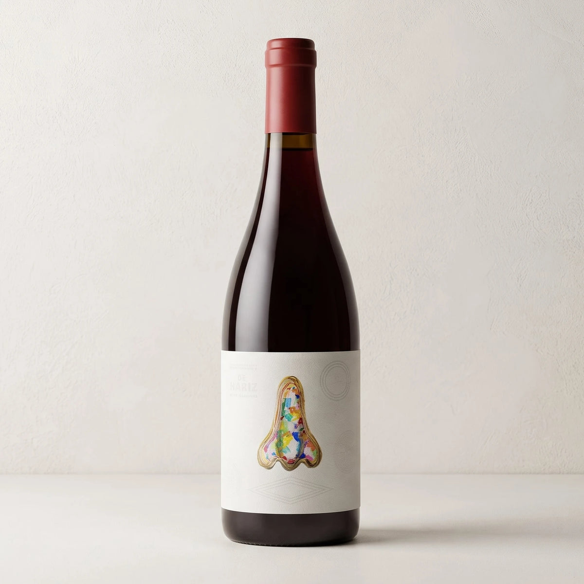 Botella de vino tinto De Nariz "La Martínez" sobre fondo de estudio, con tapón de color granate y etiqueta blanca ilustrada con un dibujo a bolígrafo de una nariz rellenado con trazos de colores en D'12 Gourmet